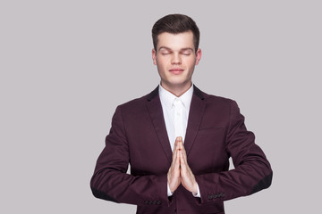 Portrait of calm handsome young man in violet suit and white shirt, standing, closed eyes with yoga...