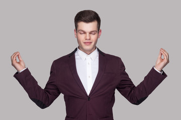 Portrait of calm handsome young man in violet suit and white shirt, standing, raised arms, closed...