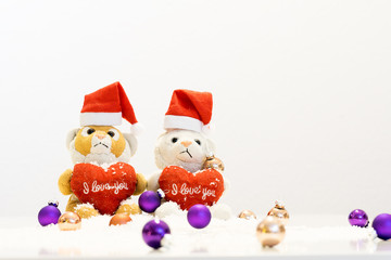 Zwei Teddybären sitzen im Schnee mit Christbaumkugeln vor weißem Hintergrund.