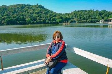 Senior women tourist Sitting on stone chair beside the Lake on top of the xiqiao mountain foshan city china