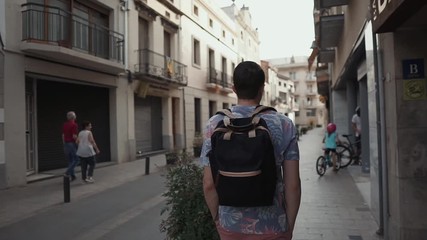 Rear view of a man with backpack taking a walk in city abroad, man sightseeing. Young male toursit enjoying city views, beautiful architecture.