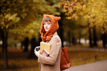 Beautiful happy smiling student girl wearing stylish knitte fox hat and camel jacket posing in...