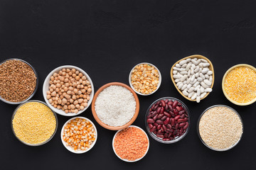 Legumes and grains in various bowls on black background