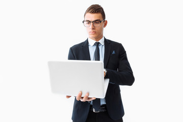 Confident man with glasses, young handsome businessman in a suit holding a laptop and looking at the screen, standing on a white background