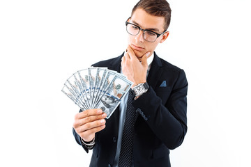 businessman in glasses and suit, holding dollar bills, looks at them carefully, on a white...