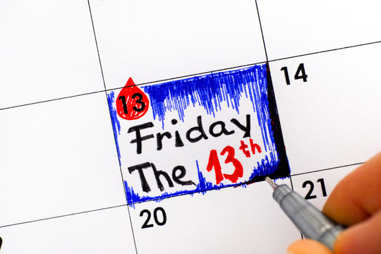 Woman fingers with pen writing reminder Friday The 13th in calendar.