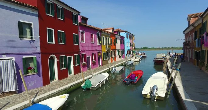 Wide shot of small motorboats moored in narrow canal with colourful houses