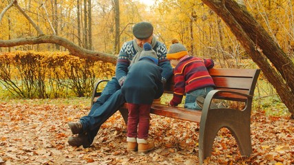 Little Boys are playing chess with grandpa on the bench in the autumn park