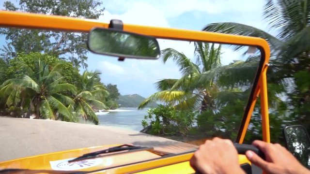 Scenic view through car windscreen while driving on remote tropical island with granite rocks, palm trees in rental mini Moke/beach buggy. Slow motion 50p.