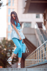 Woman Trendy Fashion. Attractive sporty asian girl in full length with elegant hairstyle. Female with perfect slim body in trendy clothes against city street. Gorgeous woman with backpack in blue