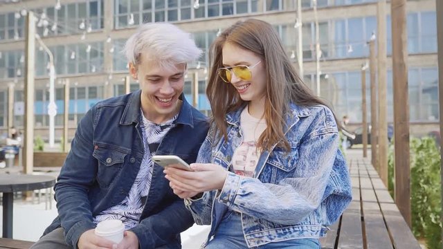 Young hipster couple smiling and having fun with a smart phone in urban background