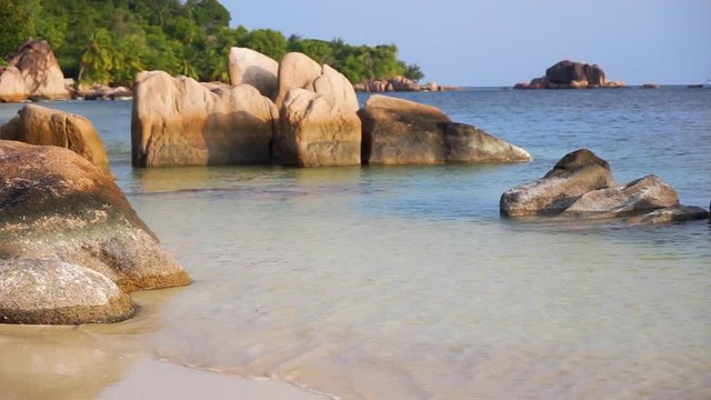 Scenic view of calm late afternoon beach and waves at Anse st. Sauveur, Praslin Island, with granite rock boulders, catamaran. Close, Slow motion 50p.