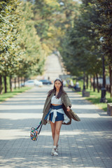 Asian woman urban fashion photo. Beautiful mixed race asian caucasian young girl in green raincoat walking outdoor against green blurred bokeh city park background. Gorgeous slim model in trendy