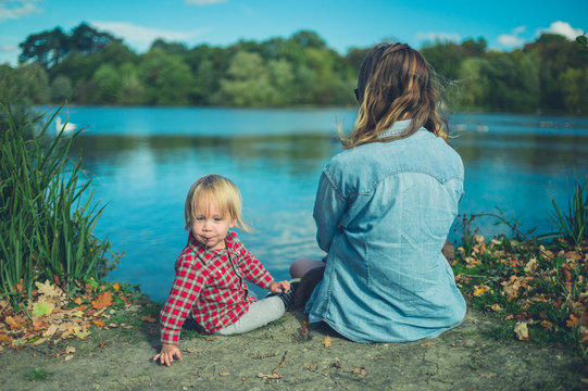 Mother and toddler relaxing by pond in forest