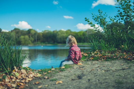 Little toddler sitting by a pond in the forest