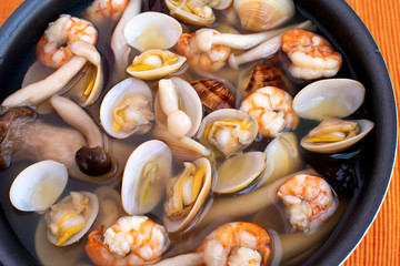 Delicious asian seafood soup with srimps, clams, enoki and soybean sprouts on orange tablecloth. Top view.