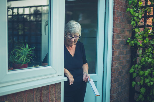 Senior woman standing in doorway with notepad