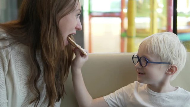 boy blond feeds his mom pizza margarita. The boy holds a slice of pizza in his hands and brings it to his mother's mouth. A young beautiful woman laughs and bites off a piece, begins to chew.