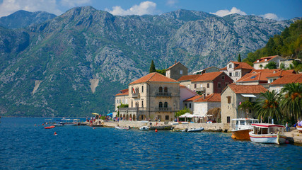 Fototapeta na wymiar Picturesque view of the water of the Bay of Kotor and the church in the town of Perast. Historic buildings and beautiful wild nature attract many tourists and water sports enthusiasts here.