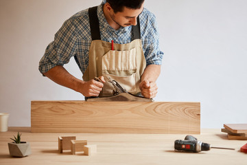 Close up of a handsome caucasian repair man planing wooden plank with a hand plane. Profession, carpentry, woodwork and people concept.