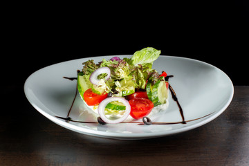 Salad with cheese and fresh vegetables on white plate.
