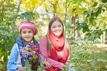 Girl with Down syndrome and little girl in autumn park.