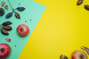 Pomegranates and dry leaves on yellow and green background. Creative Autumn layout. Border arrangement. Flat lay top view. Copy space.