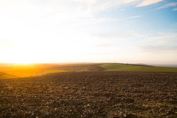 Ditchling Beacon, Sussex, UK. A strong orange sun prepares to set behind the rolling hills of Sussex. Plouged field in foreground.