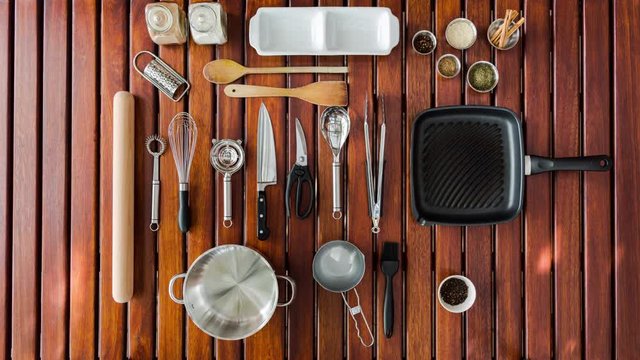 Stop motion timelapse of important kitchen utensils and cooking items displayed in a neat overhead/flat lay manner on a wooden table. 4K, 25p.