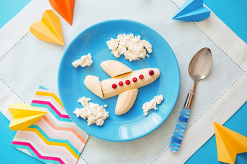 Fun food idea for kids. children's Breakfast: plane made of banana and clouds made of curd on a blue plate. dreams of flying. creative lunch of the future pilot