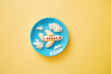 Fun food idea for kids. children's Breakfast: plane made of banana and clouds made of curd on a blue plate. dreams of flying. creative lunch of the future pilot