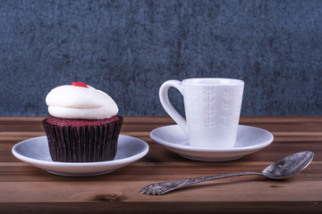 Fototapeta na wymiar Red velvet Cupcake and white cup (mug) of espresso coffee next to old vintage spoon on wood table on blue grunge background.