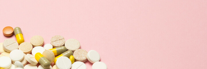 Pills of different sizes and colors on a light pink background.