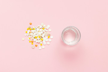Pills of different sizes and colors and Glass of water on a ligh
