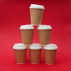 Six paper cups with coffee on a red background