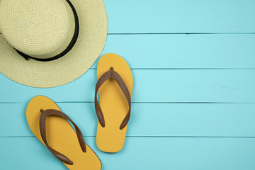 Straw hat and flip flops on light green wooden background.