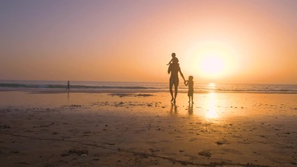 Silhouette of father with two children in the beach at sunset