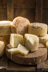 Assorted caciotta cheese on wooden board on dark background