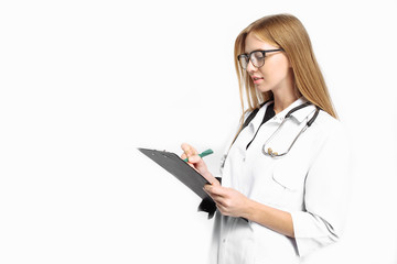 A young girl trainee, with glasses, with a stethoscope around her neck, writes the diagnosis in her folder, on a white background.