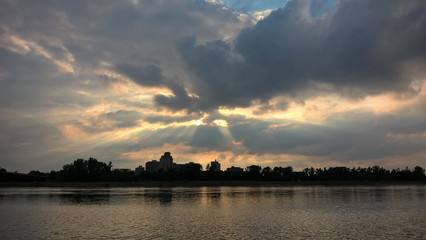 Fototapeta premium Sonnenuntergang am Flussufer mit Sonnenstrahlen im Himmel