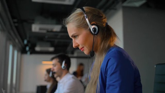 Young businesswoman talking on headset with colleagues. Attractive businesspeople speaking with customers. Beautiful co-working office building skyscraper. Slow motion close-up.