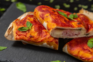 Closed calzone pizza with dry-cured ham, mozzarella cheese, Basil and tomatoes