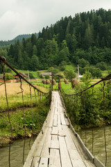 Fototapeta premium Old suspension bridge crossing mountain river. Landscape view