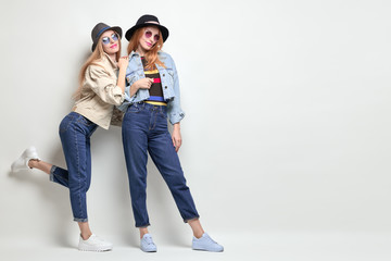 Two Playful Friends Having Fun in Studio. Young Beautiful Hipster Girl in Stylish jacket, jeans....