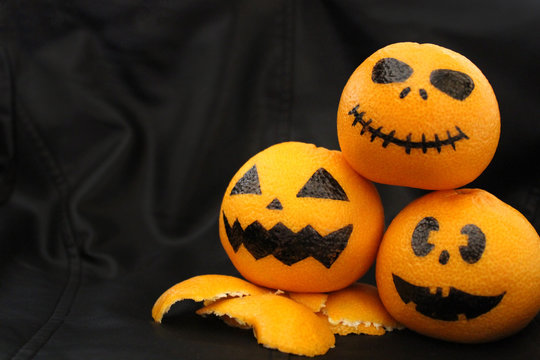 Halloween concept. Funny orange mandarins or tangerines pumpkin painted in the form of icons of Halloween on a black background. Painted scary faces on a holiday of halloween.