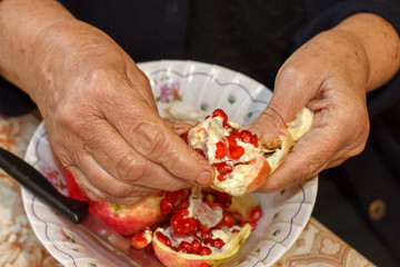 Hands of an elder woman peeling off pomegranates in a plate