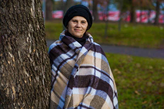 Attractive middle aged woman covered with blanket walk in autumn park