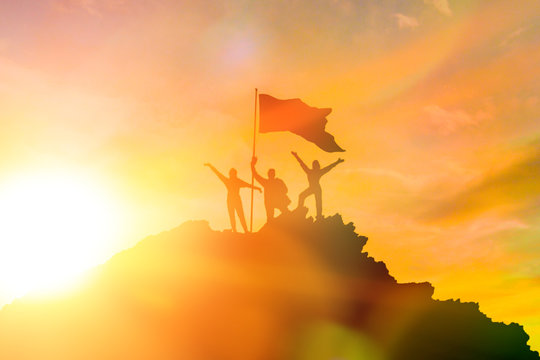 High achiever, silhouettes of three people holding on top of a mountain to raise their hands up. A man on top of a mountain. Conceptual design. Against a dramatic sky with clouds at sunset.