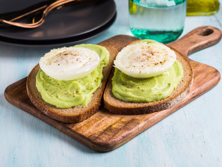 Rye bread avocado toasts with poached egg on wooden serving board. Brunch lunch meal