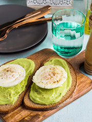 Rye bread avocado toasts with poached egg on wooden serving board. Brunch lunch meal